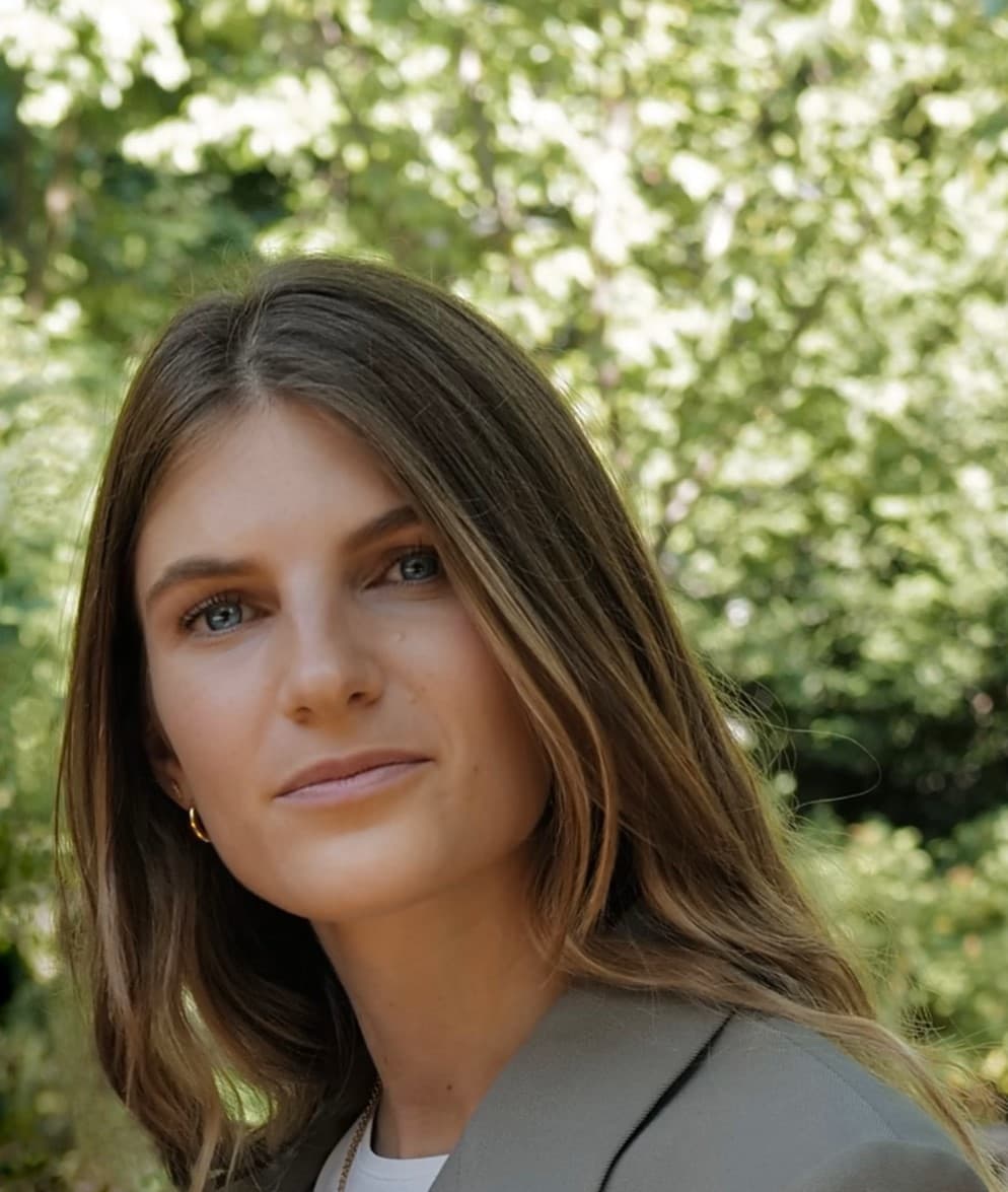 Junge Frau mit langen braunen Haaren und blauen Augen vor einem unscharfen grünen Hintergrund.