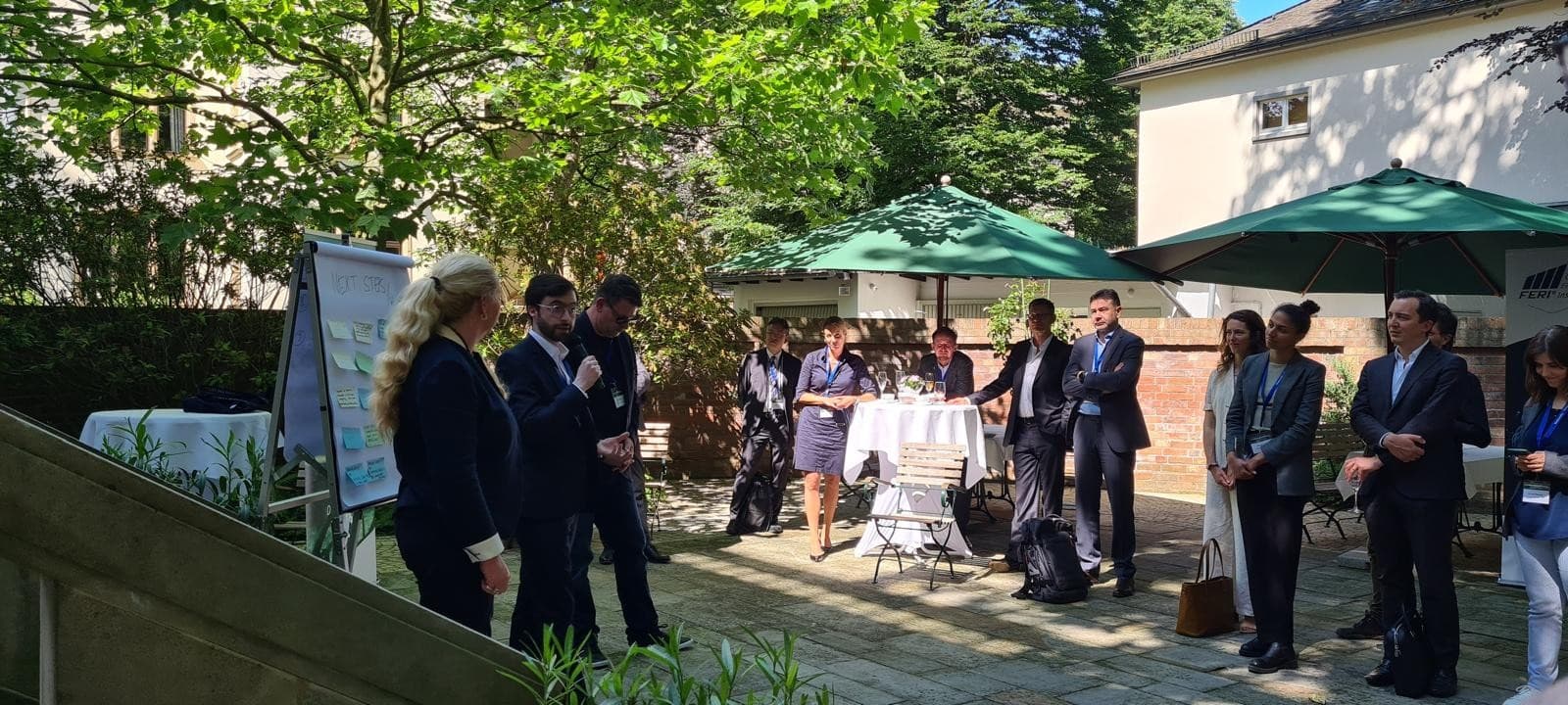 Geschäftsleute bei einer Präsentation im Freien mit Whiteboard und grünen Sonnenschirmen in einem Garten.